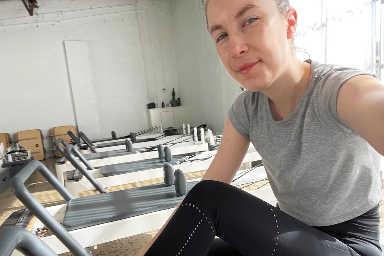 A person sitting on a pilates reformer in a brightly lit studio